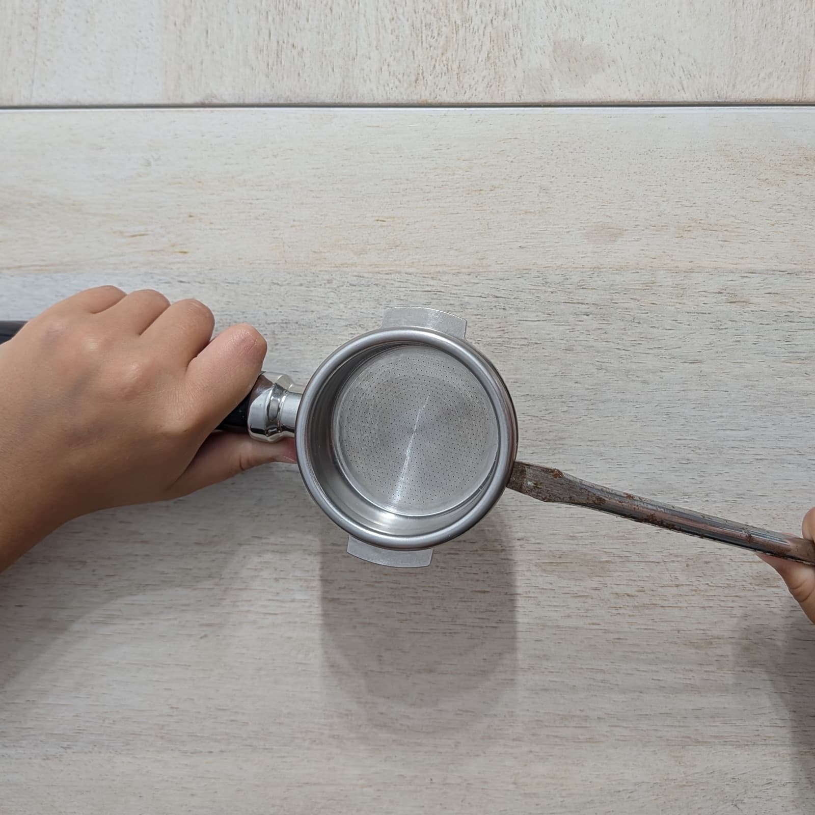 A screwdriver being used to pry a basket out of a portafilter.