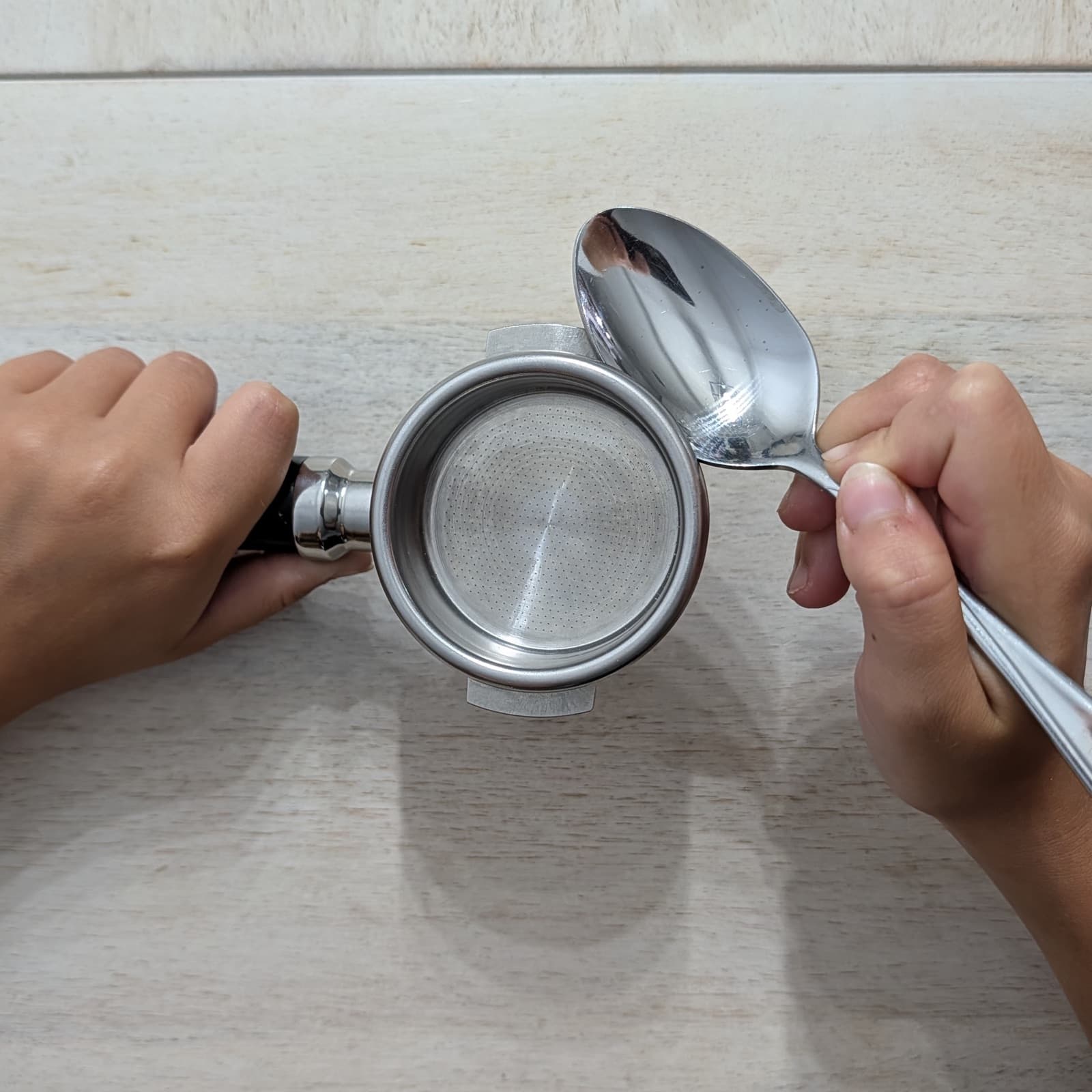 A spoon being used to pry a basket out of a portafilter.